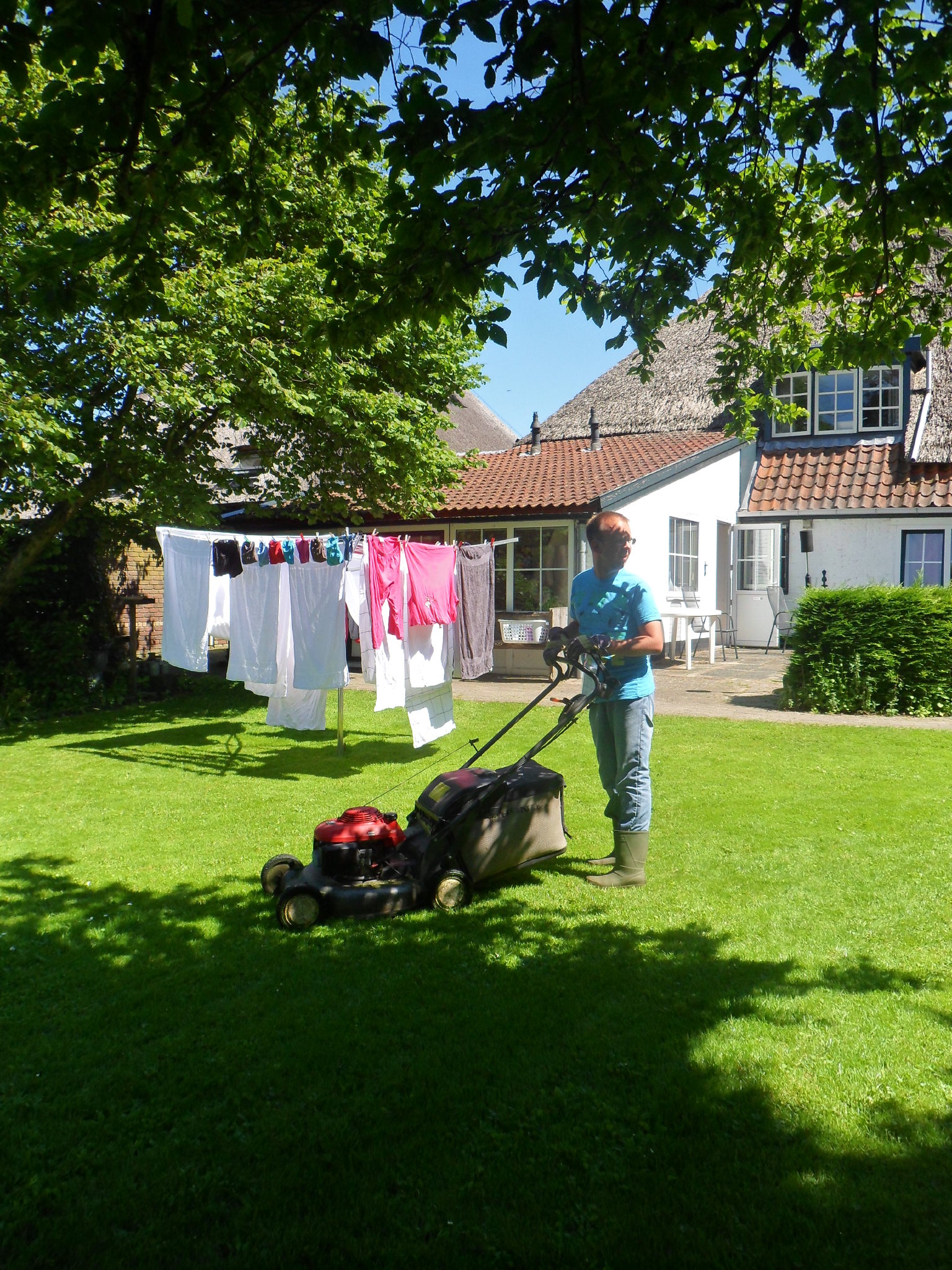 Een bewoner maait het gras bij de boerderij, naast de waslijn